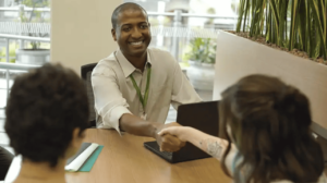 Agente financeiro sorri e aperta a mão de novos associados na cooperativa Sicredi