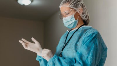 Profissional com EPI hospitalar ajusta luvas, usando máscara, óculos e avental